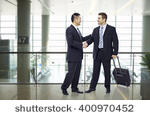stock-photo-two-businessmen-one-asian-and-one-caucasian-shaking-hands-and-smiling-at-modern-airport-400970452
